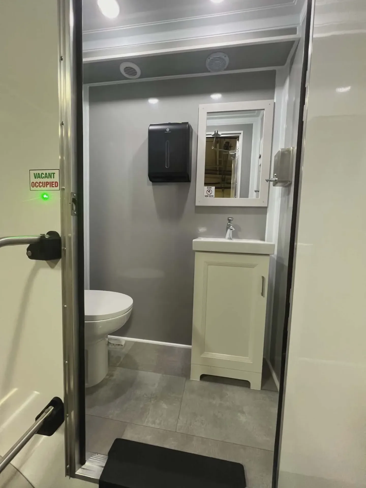 Inside a private stall of the restroom trailer with porcelain toilet, vanity sink and mirror