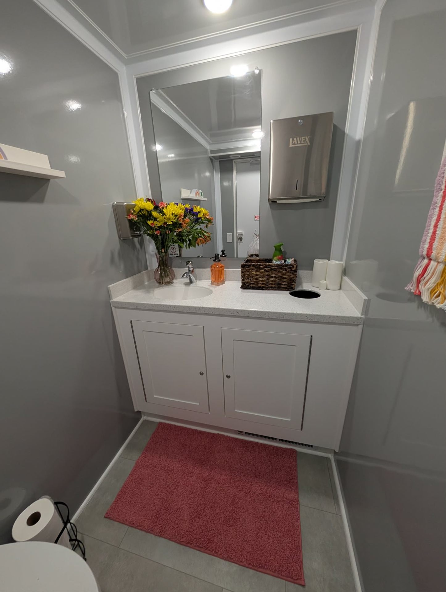 Interior of The Social Stall restroom trailer showing white vanity, framed mirror and fresh florals
